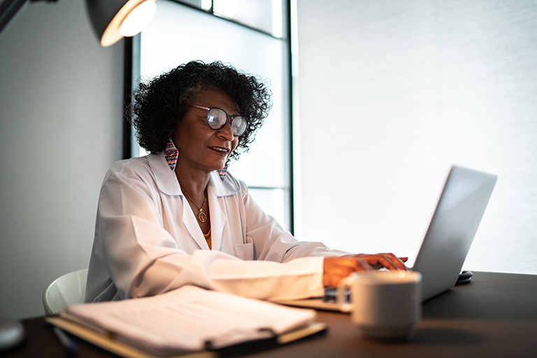 Doctor sitting at her desk typing on her laptop.